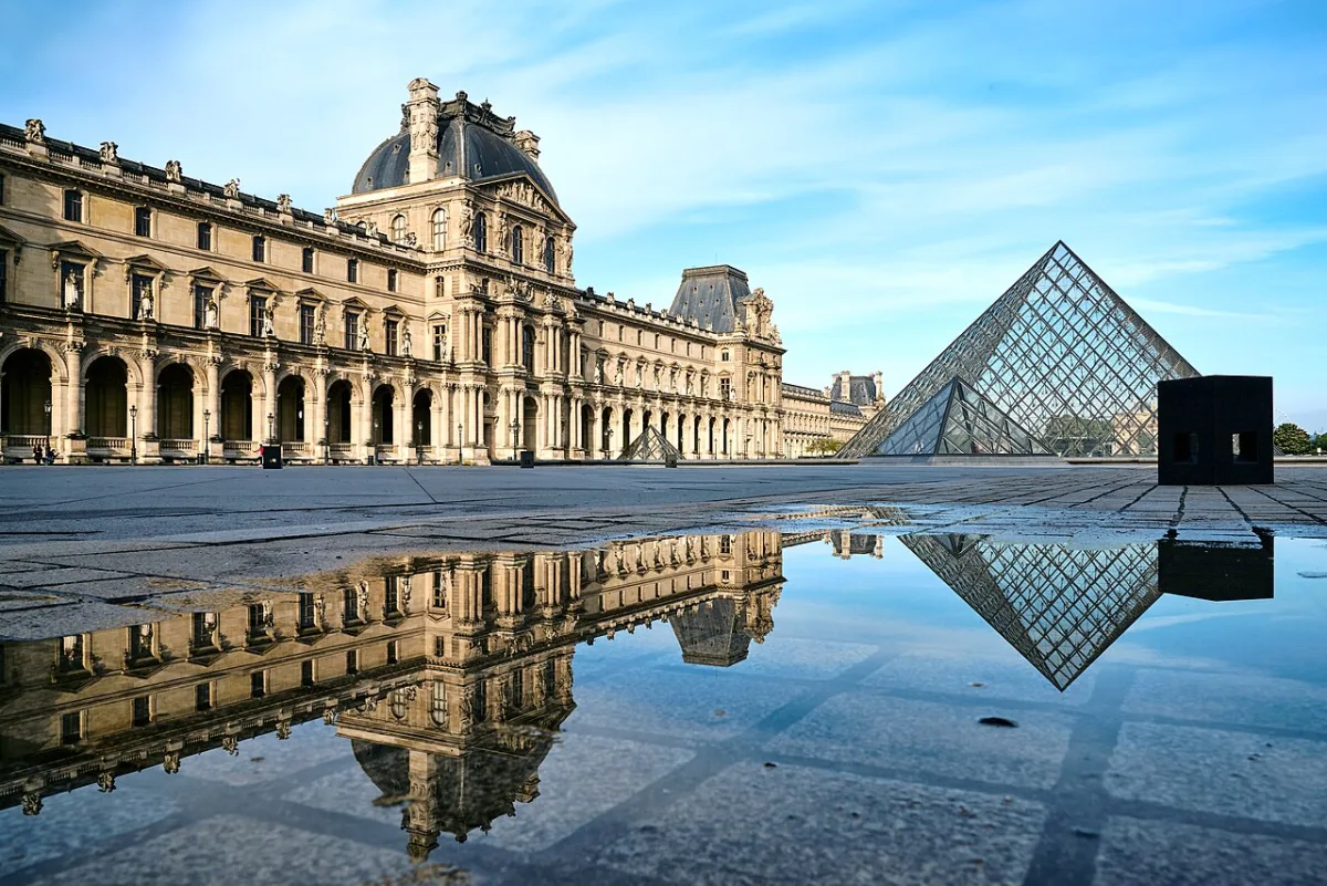 De glazen piramide van het Louvre overdag met het paleis op de achtergrond en een spiegeling in een plas
