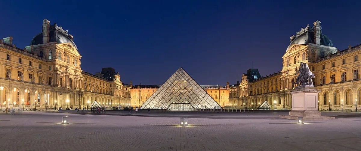 De verlichte glazen piramide van het Louvre tussen de paleisvleugels in de avondschemering